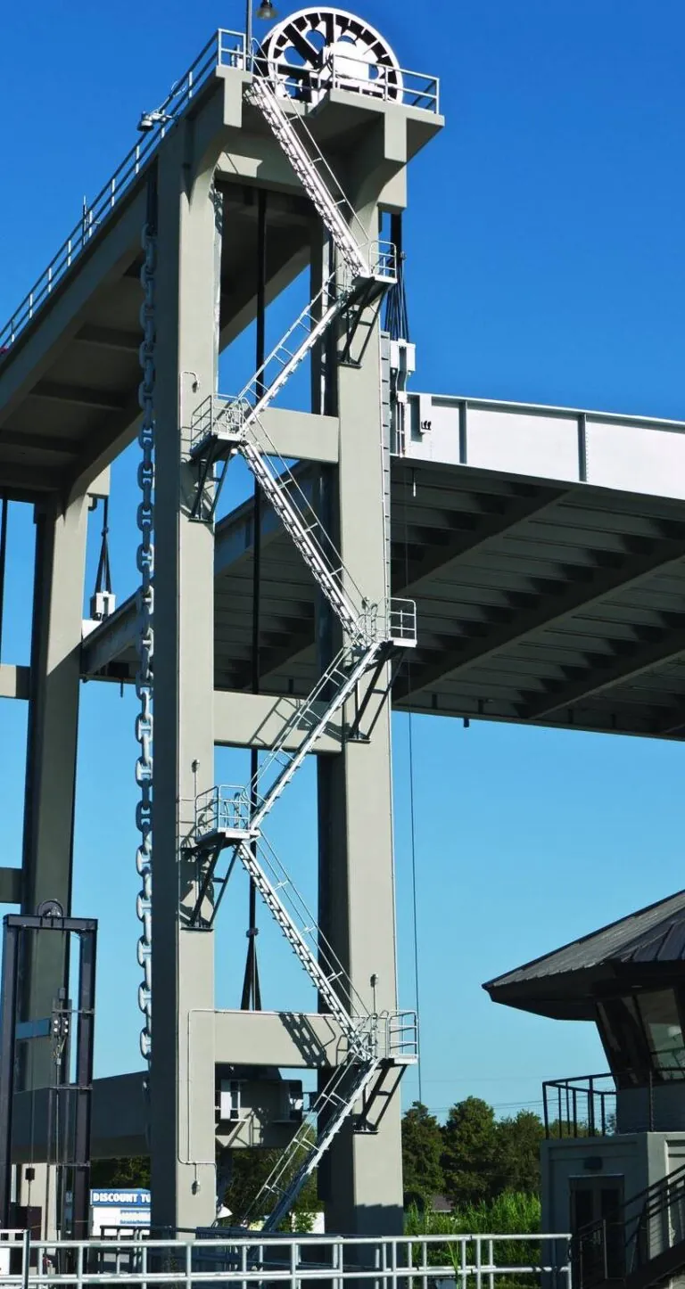 tall clock tower sitting under a bridge with industrial stairs nearby